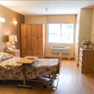 A spacious and well-lit hospital patient room with essential furniture and a view outside.
