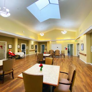 A spacious and well-lit communal area with tables and chairs, featuring a skylight and hardwood flooring.
