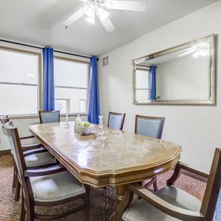 A cozy dining room with a wooden table, surrounded by chairs, featuring blue curtains and a large mirror.