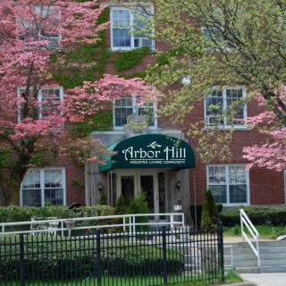 The entrance of a brick building adorned with spring blossoms and a green awning labeled 'Arbor Hill'.
