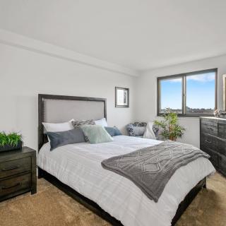 A minimalist bedroom featuring a neatly made bed, a dresser, and potted plants with natural light coming through the window.