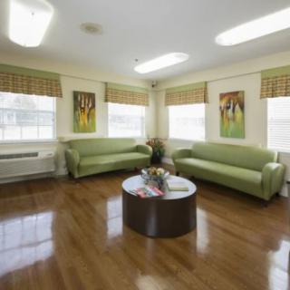 A well-lit waiting room with green sofas, a central table, and artwork on the walls.