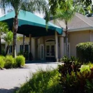 A building entrance with a green awning surrounded by lush greenery and palm trees.
