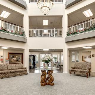 A spacious and elegantly designed lobby with sofas, a central round table, and a chandelier.