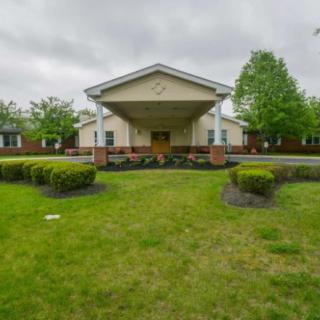 A front view of a building entrance surrounded by greenery and trees under a cloudy sky.