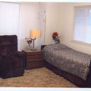 A cozy bedroom with a single bed, recliner chair, and side table featuring a lamp and flower vase.