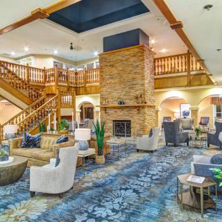 A spacious hotel lobby with a central fireplace, comfortable seating, and a grand staircase.