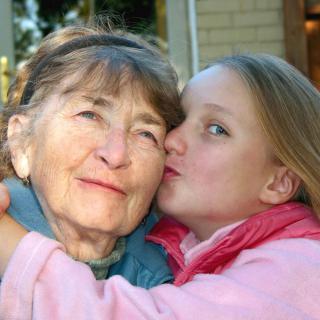 A young girl affectionately kisses her grandmother outdoors.