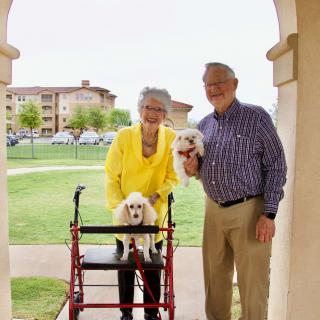 An elderly couple smiling with their two small dogs outdoors.
