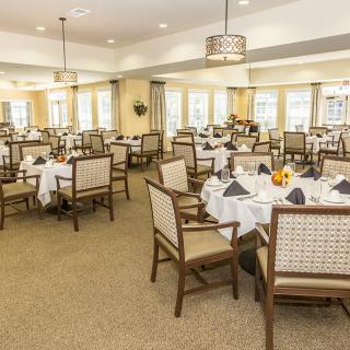 A well-decorated dining room with multiple tables set elegantly with white tablecloths and chairs.