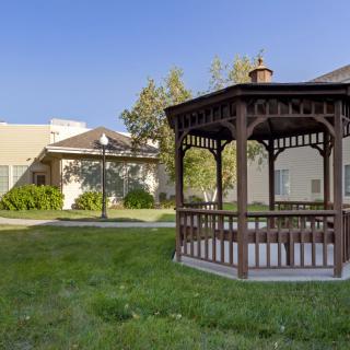 A wooden gazebo situated in a sunny garden with green grass and trees.
