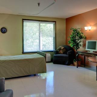 A cozy bedroom featuring a bed, desk with a computer, chair, and large window.