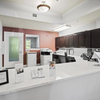 A modern reception area with a sleek white desk, office equipment, and dark cabinetry.
