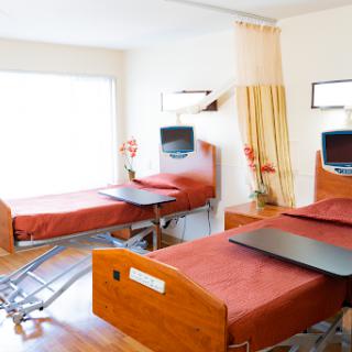 A modern patient room featuring two hospital beds with red bedding and equipped with televisions.