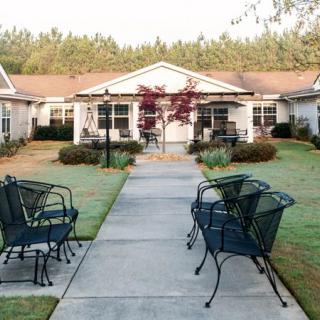 A peaceful outdoor area with chairs lining a pathway leading to residential buildings surrounded by lush landscaping.