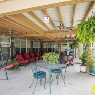 A cozy outdoor patio with red cushioned chairs, a swing, and greenery under a covered roof.