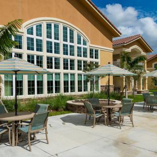 Outdoor patio area with tables, chairs, and umbrellas near a large building with arched windows.