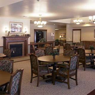 A cozy dining area featuring round tables with patterned chairs, a carpeted floor, and a fireplace surrounded by wooden decor.
