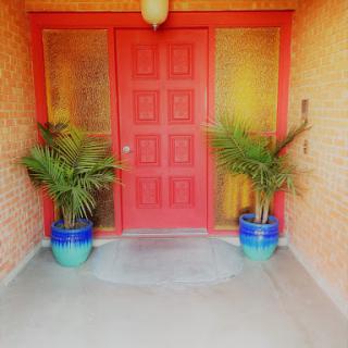A welcoming entrance featuring a vibrant red door and potted plants on either side.