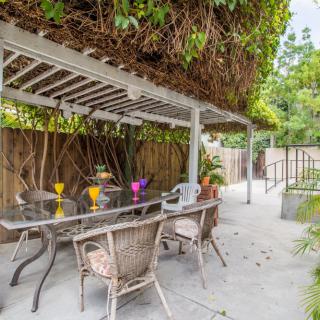 A cozy outdoor patio with a pergola and seating area, surrounded by lush greenery.