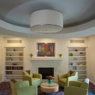 A modern living room featuring a circular seating arrangement around a central table, with a fireplace and built-in shelves on the wall.