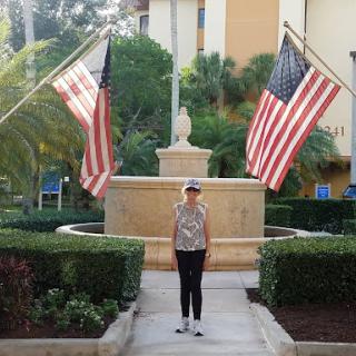A person standing in front of a fountain, flanked by American flags.