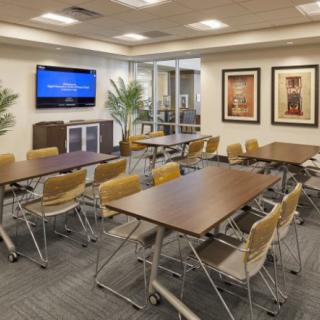 A modern conference room equipped with tables, chairs, a television, and indoor plants.