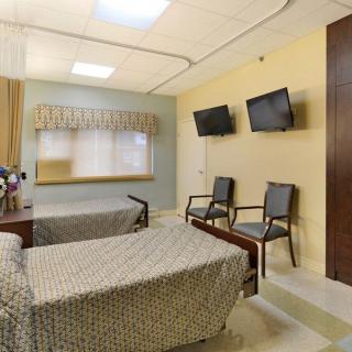 A hospital room featuring two beds, televisions, and seating for patients or visitors.