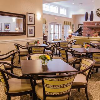 A cozy dining area with neatly arranged tables and chairs, decorated with flowers and artwork on the walls.