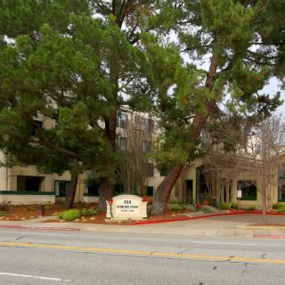 A view of a building with a sign at the entrance, surrounded by trees and adjacent to a road.