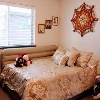 A cozy bedroom with a decorated daybed, plush pillows, and teddy bears, featuring wall art and framed photos.