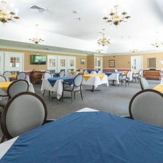 An elegantly set dining room with multiple tables and chairs, featuring chandeliers and colorful tablecloths.