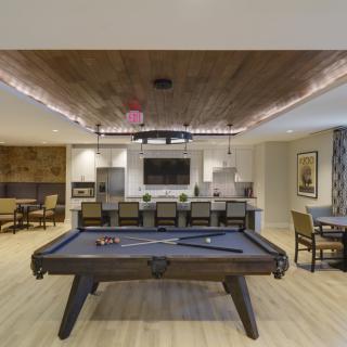 A modern entertainment room featuring a pool table and kitchen area.