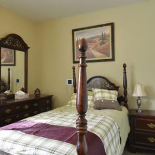 A cozy bedroom with a wooden four-poster bed and matching dresser, featuring classic decor and a landscape painting on the wall.