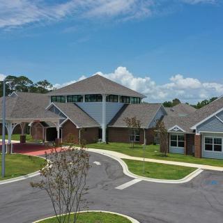 A large educational facility with a brick exterior and multiple interconnected sections under a blue, cloudy sky.