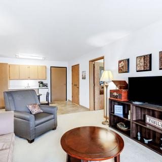 A cozy living room with comfortable seating, a television, and a view into the adjoining kitchen.