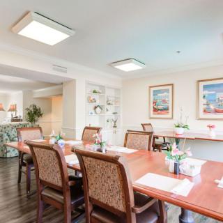 A bright and inviting dining room with a large wooden table surrounded by chairs, decorated with artwork on the walls.