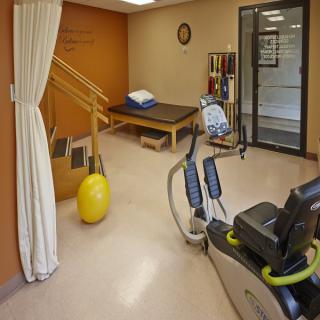 A physical therapy room with exercise equipment, including a stationary bike and yellow exercise ball.