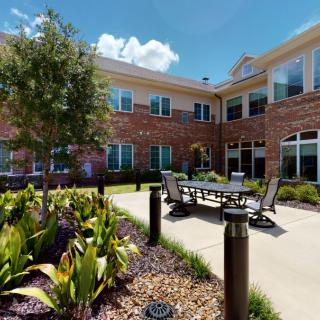 A sunny courtyard with outdoor seating and a landscaped garden in front of a brick building.