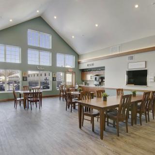 A spacious and modern dining area with multiple tables and chairs, featuring a high ceiling and large windows.