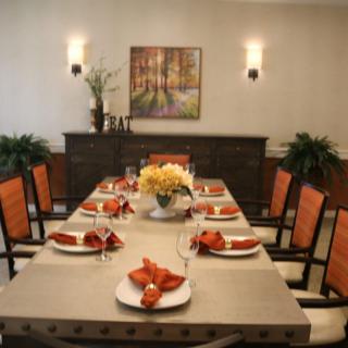 A well-decorated dining room with a neatly set table, featuring red napkins, a floral centerpiece, and warm lighting.