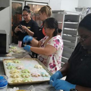 A group of people working together in a kitchen to prepare colorful treats.