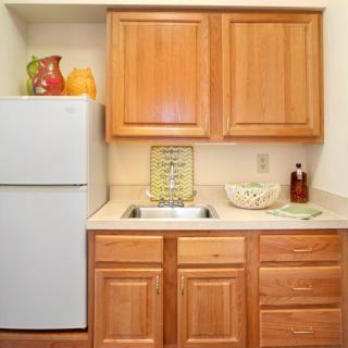 A compact kitchen with wooden cabinets, a refrigerator, and decorative items on the countertop.