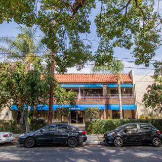 A street view featuring parked cars in front of a building surrounded by trees.