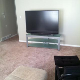 A living room with a television on a glass stand and carpet flooring.