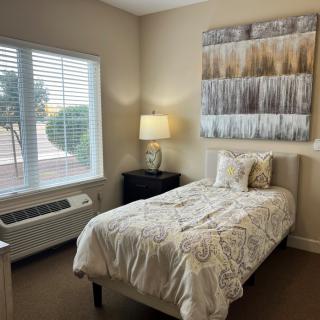A cozy bedroom with a single bed, lamp, and abstract wall art.