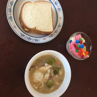 A meal featuring a bowl of soup, slices of bread on a plate, and a cup of colorful dessert.