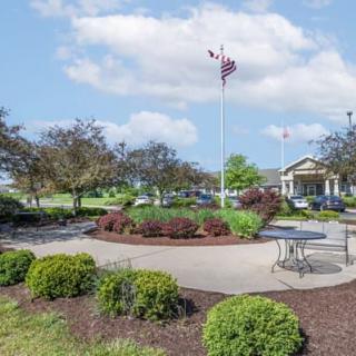 A scenic view of a landscaped park area with benches, surrounded by greenery and a flagpole under a partly cloudy sky.