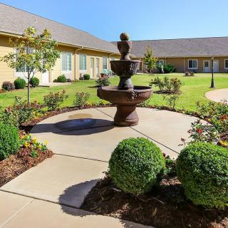 A beautifully landscaped courtyard featuring a central fountain surrounded by manicured shrubs and pathways.