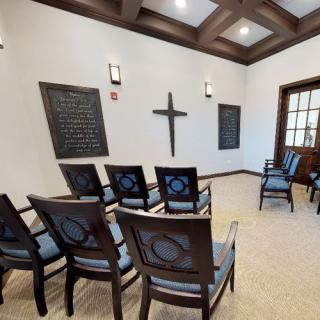 A small chapel interior with a cross on the wall and arranged chairs.